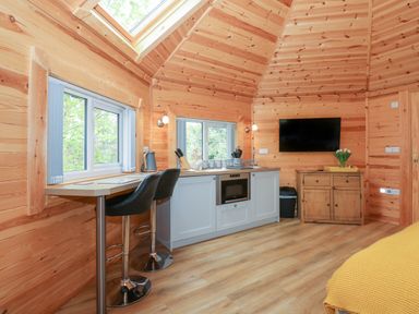 A kitchen area with bar stools oven and a wooden cabinet with a television mounted above at Honeybee Retreat in Pentney near Upper Marham
