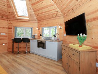 A wooden kitchen with two black stools a TV on a wooden sideboard and a skylight window at Honeybee Retreat in Pentney near Upper Marham