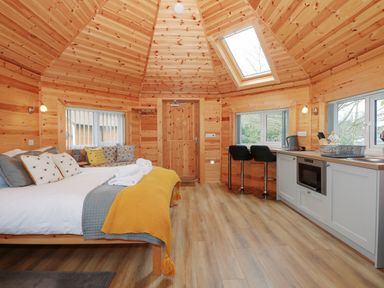 A wooden cabin interior with a bed a kitchenette and bar stools at Honeybee Retreat in Pentney near Upper Marham