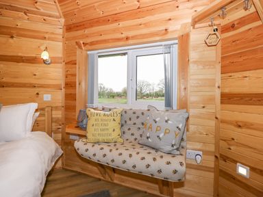 A bedroom with wooden walls a bed a window seat with bee patterned cushions at Honeybee Retreat Pentney near Upper Marham