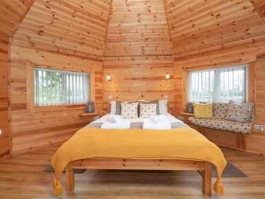 A bedroom with wooden walls a bed with white towels and yellow blanket and windows with vertical blinds at Honeybee Retreat in Pentney near Upper Marham