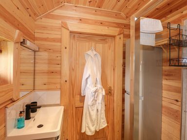 A bathroom with a white sink black faucet a white bathrobe hanging on a wooden door and towels on a rack at Honeybee Retreat in Pentney near Upper Marham
