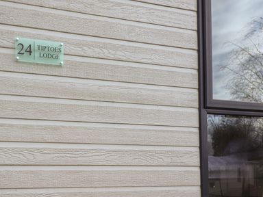 The exterior wall of a building with a house number 24 and tiptoes lodge sign next to a window reflecting trees and sky at Tiptoes Lodge in Carnforth