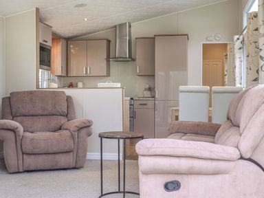 A living area with a brown armchair a beige sofa a small round table and a kitchen with cabinets and appliances at Tiptoes Lodge in Carnforth