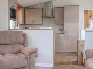 A kitchen with beige cabinets a stainless steel extractor fan a microwave and a knife set next to a living area with a brown armchair at Tiptoes Lodge in Carnforth
