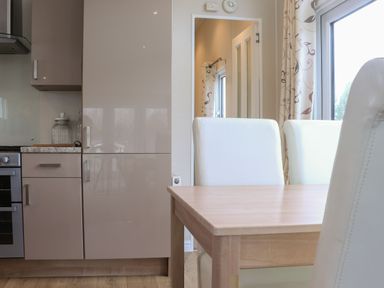 A kitchen with beige cabinets a wooden dining table and white chairs near a window at Tiptoes Lodge in Carnforth