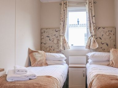 A bedroom with two single beds with pillows and cushions and a window with curtains at Tiptoes Lodge in Carnforth