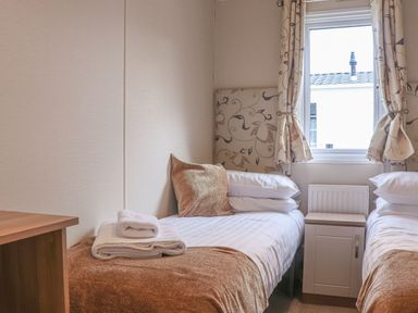 A bedroom with two single beds a window between them and a small cabinet at Tiptoes Lodge in Carnforth