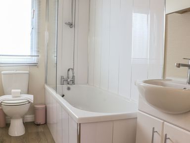 A bathroom with a bathtub shower combination a toilet and a sink with cabinet at Tiptoes Lodge in Carnforth