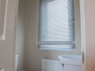 A bathroom with a window covered by blinds a toilet a radiator and a sink at Tiptoes Lodge Carnforth