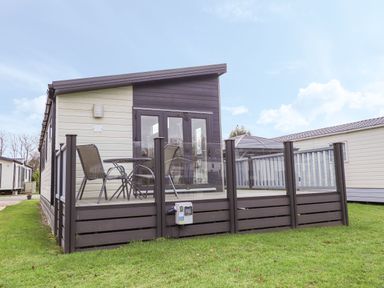 A modern cabin with a small deck with glass railing and outdoor chairs and table at Tiptoes Lodge in Carnforth