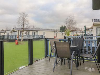 An outdoor deck with a round table and four chairs overlooking multiple mobile homes at Tiptoes Lodge in Carnforth
