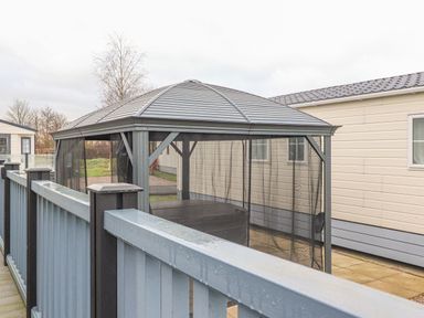 A gazebo with mesh sides on a paved patio next to a cream-colored building at Tiptoes Lodge in Carnforth