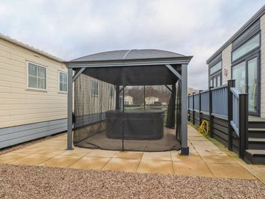 An outdoor hot tub under a gazebo with mesh sides between two mobile homes at Tiptoes Lodge in Carnforth
