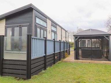 An exterior view of a building with a fenced patio and a gazebo covering a hot tub at Tiptoes Lodge in Carnforth