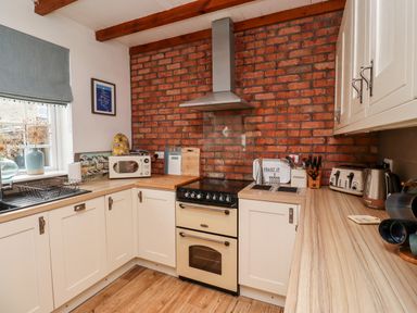 A kitchen with white cabinets wooden countertops a brick wall oven microwave toaster kettle and a window with a blind at Seahares in Seahouses