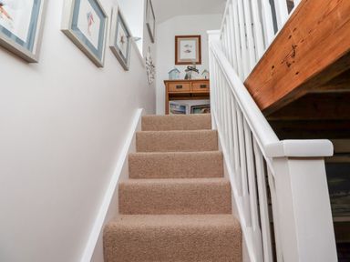 A carpeted staircase with framed pictures on the wall and a wooden table with decorations at the top at Seahares in Seahouses