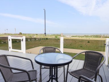A deck area with a table and chairs overlooking grass and the sea at Bonny Bay Wilsthorpe near Bridlington