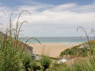 A view of the beach and ocean from a hillside with houses and plants in Clematis House in St Columb Major