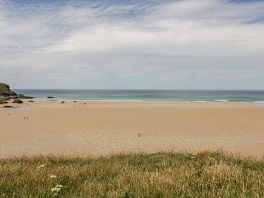 A wide sandy beach with sparse people and grassy dunes by the sea at Clematis House in St Columb Major