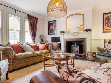 A living room with sofas, a fireplace, a mirror above it, a wooden coffee table, and framed pictures at Clematis House in St Columb Major