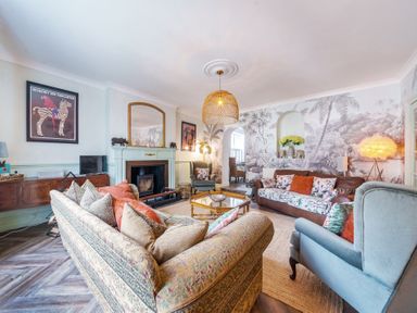 A living room with patterned sofas a fireplace a wall mural and a hanging light at Clematis House in St Columb Major