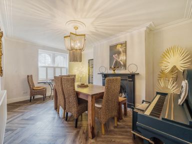 A dining room with wooden table and wicker chairs a piano and fireplace at Clematis House in St Columb Major
