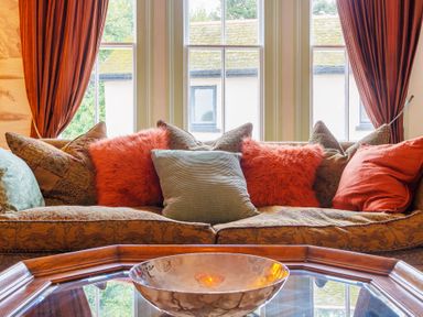 A sofa with multiple pillows in front of windows with curtains at Clematis House in St Columb Major