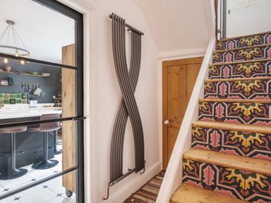 A hallway with a patterned tiled staircase next to a door and a view of a kitchen with bar stools at Clematis House in St Columb Major