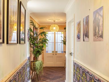 A hallway with patterned lower wall panels plants framed pictures and double doors with frosted glass at Clematis House in St Columb Major
