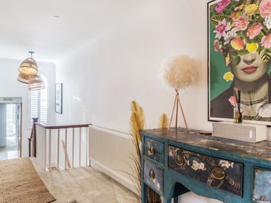 A hallway with a decorated chest of drawers a feather lamp and floral artwork at Clematis House in St Columb Major