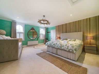 A bedroom with a bed a sofa a wooden slatted accent wall a round mirror and green walls at Clematis House in St Columb Major