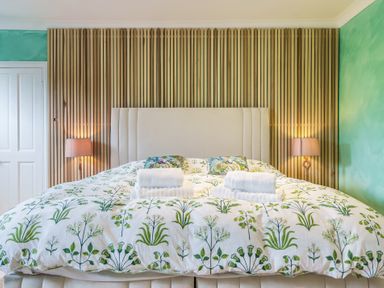 A bedroom with a large bed with botanical bedding and folded towels on top at Clematis House in St Columb Major