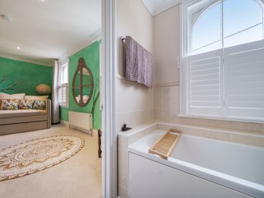 A bathroom with a bathtub and towel next to a green painted sitting area with a sofa and round rug at Clematis House in St Columb Major