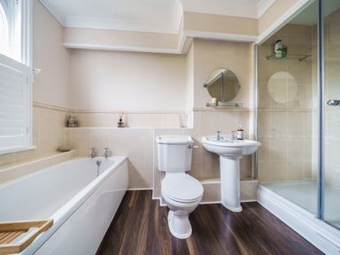 A bathroom with a bathtub, toilet, sink, glass shower enclosure and wooden floor at Clematis House in St Columb Major
