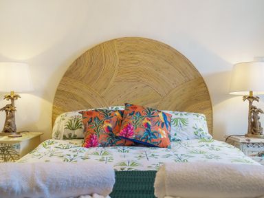 A bed with patterned pillows and a large wooden headboard with two bedside tables and lamps at Clematis House in St Columb Major