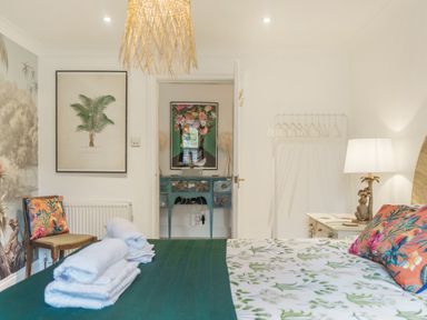 A bedroom with a bed covered in floral bedding and towels a chair and artwork at Clematis House in St Columb Major