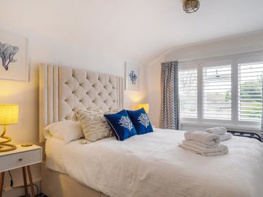 A bedroom with a bed two bedside tables with lamps and windows with shutters at Clematis House in St Columb Major