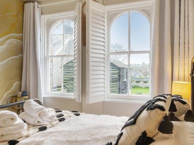 A bedroom with white shutters on windows and towels on the bed at Clematis House in St Columb Major