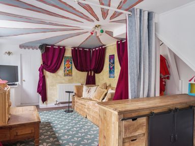 A living room with a beige sofa red curtains a wooden table and a TV at Clematis House in St Columb Major