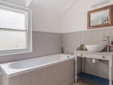 A bathroom with a bathtub under a frosted window and a washbasin with a mirror above at Clematis House in St Columb Major