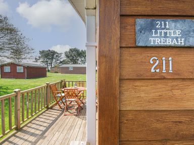 A wooden deck with a table and chairs outside wooden cabins at Little Trebah Atlantic Bays Holiday Park near St Merryn