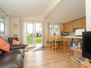 A living room with a black leather sofa and wooden dining table next to kitchen cabinets at Little Trebah Atlantic Bays Holiday Park near St Merryn
