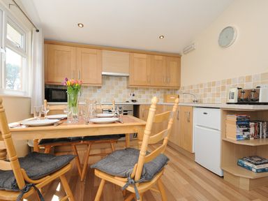 A kitchen with a wooden dining table set with plates and glasses and wooden cabinets at Little Trebah in Atlantic Bays Holiday Park near St Merryn
