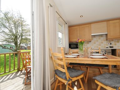A dining area with a wooden table set for four and kitchen cabinets in the background at Little Trebah Atlantic Bays Holiday Park near St Merryn
