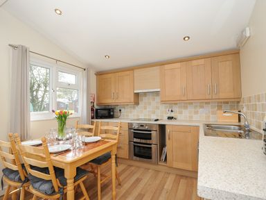 A kitchen with wooden cabinets and a dining table set with dishes and glasses at Little Trebah Atlantic Bays Holiday Park near St Merryn