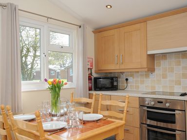 A kitchen with a wooden dining table set with plates glasses and a vase of flowers at Little Trebah Atlantic Bays Holiday Park near St Merryn