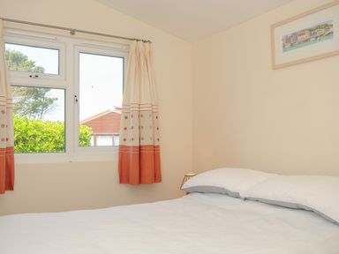 A bedroom with a bed curtains on a window and a framed picture on the wall at Little Trebah Atlantic Bays Holiday Park near St Merryn