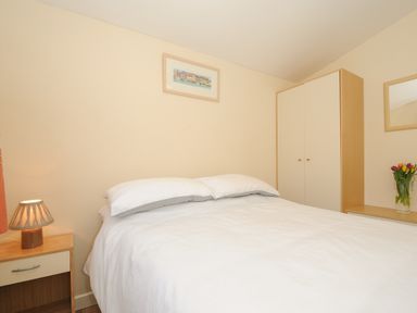 A bedroom with a bed white bedding a lamp on a bedside table a wardrobe and flowers on a dresser at Little Trebah Atlantic Bays Holiday Park near St Merryn