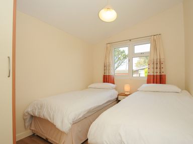 A bedroom with two single beds a window with curtains and a bedside table with a lamp at Little Trebah Atlantic Bays Holiday Park near St Merryn